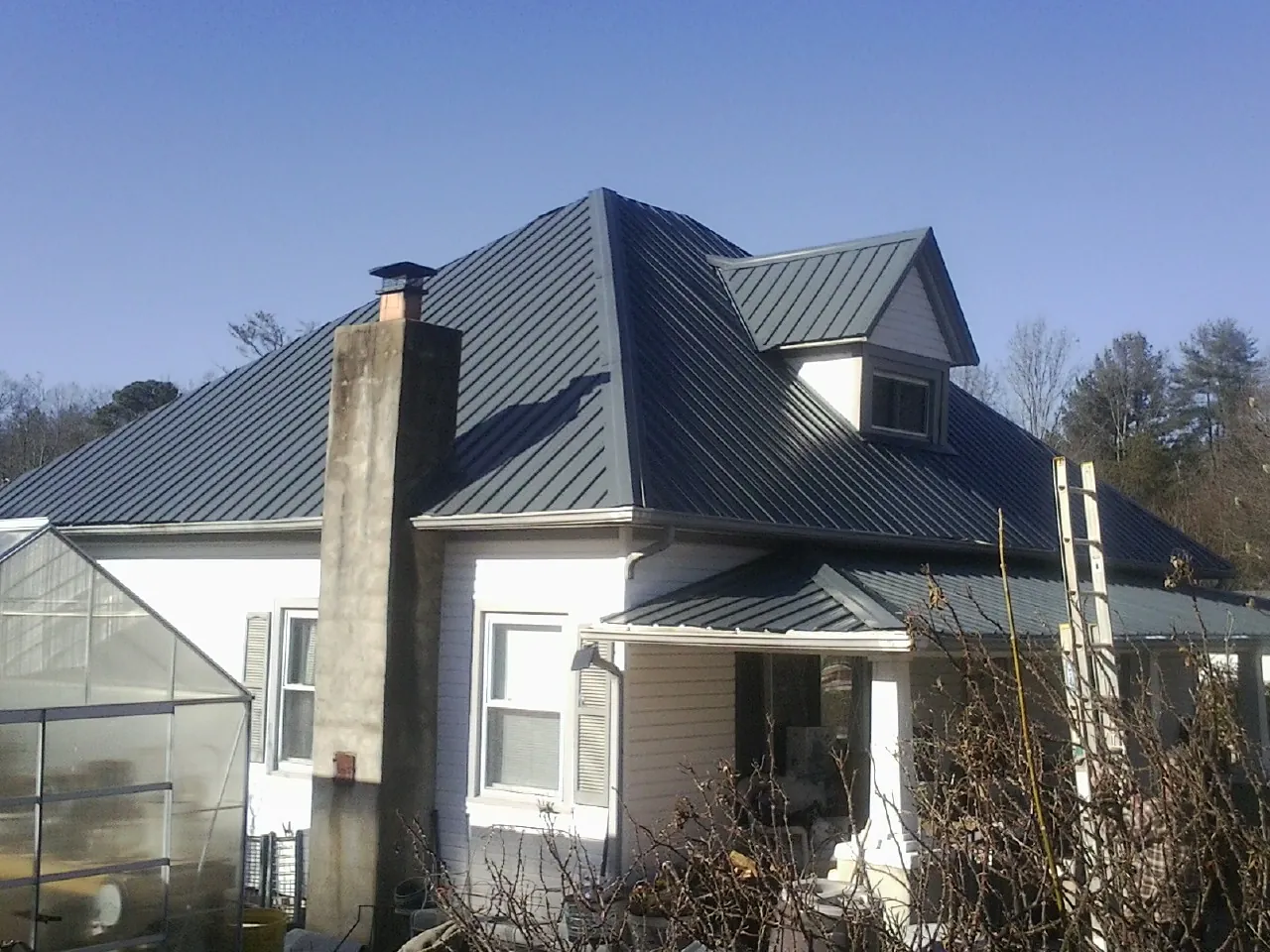 Dark blue standing seam metal roof on a white farmhouse with dormer — Slate & Tile Roof Repair by Roofing Brothers in North Troy