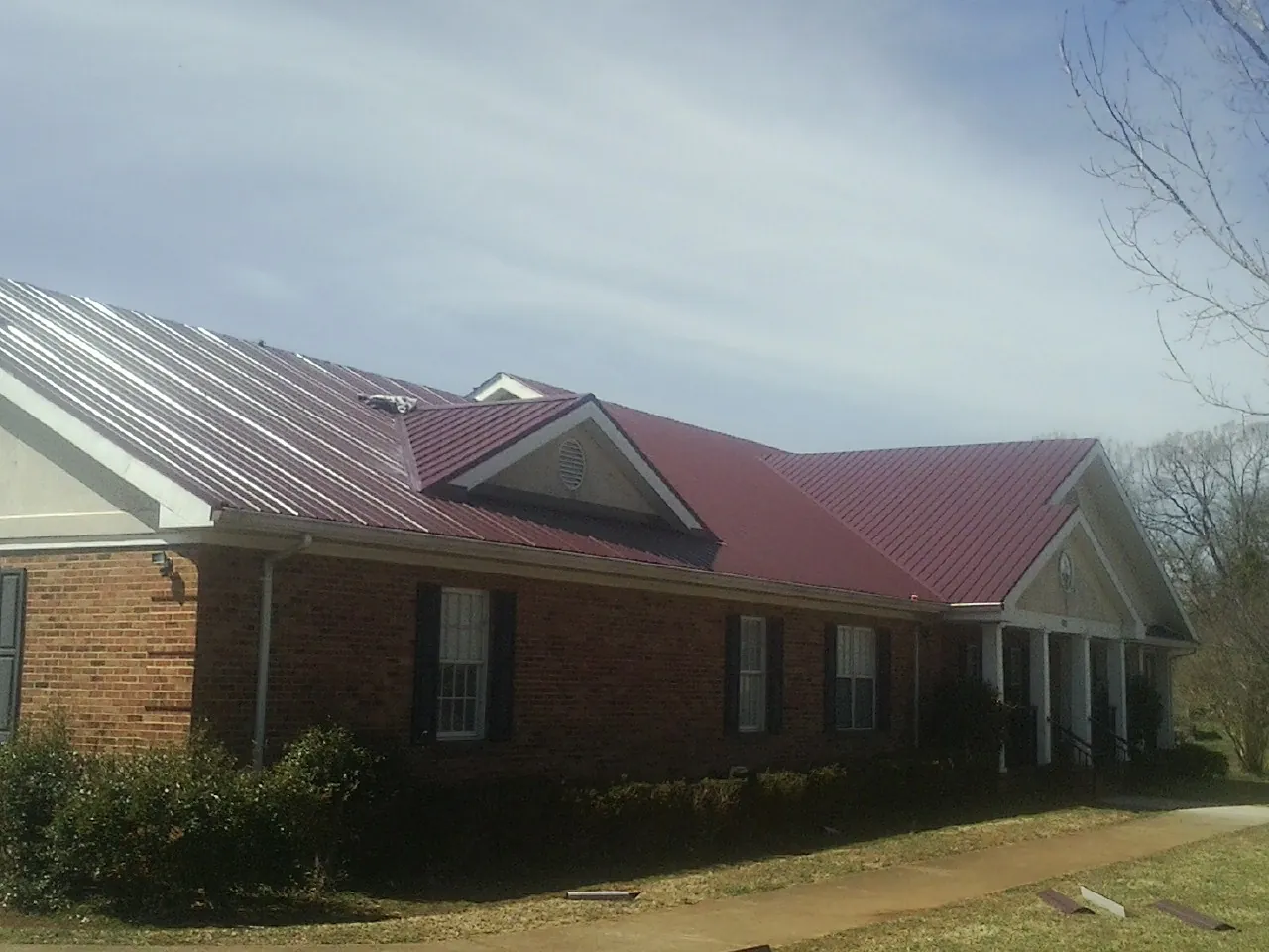 Red metal roof with gabled entries on a long brick building, from a Hail Damage Roof Repair job in North Troy