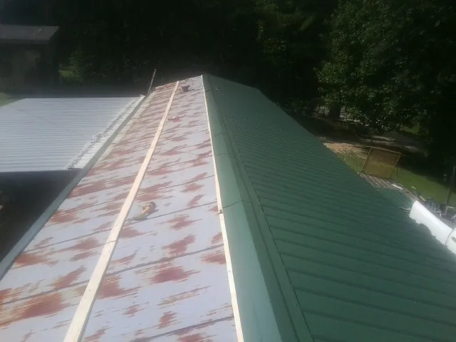 Old rusted panels beside newly installed green metal roofing — Wind Damage Roof Repair by Roofing Brothers in North Troy