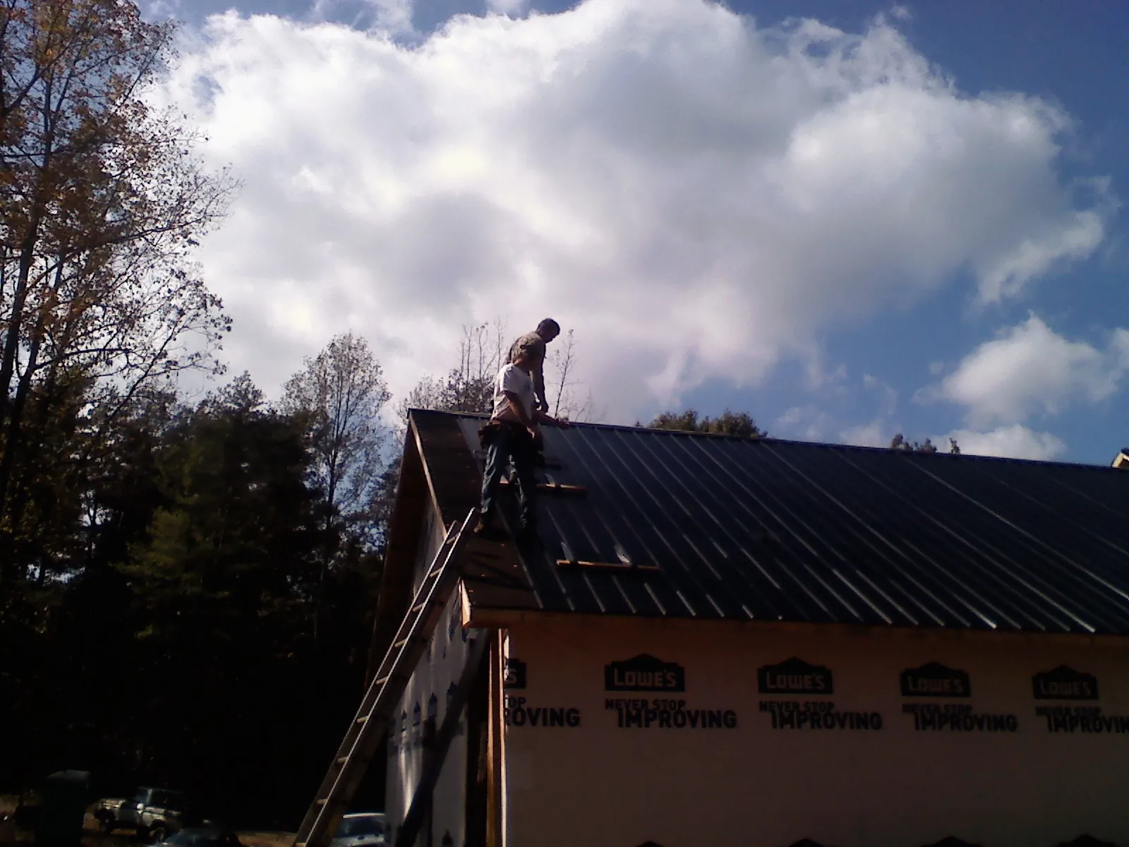 Roofer fastening dark metal panels high against a cloudy sky, from a Roof Inspection job in North Troy